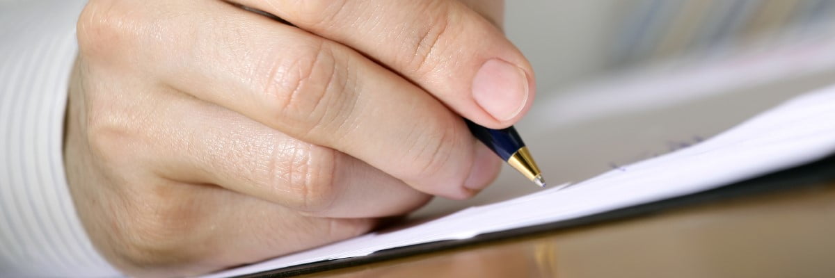 Hand som håller i bläckpenna och skriver på papper.